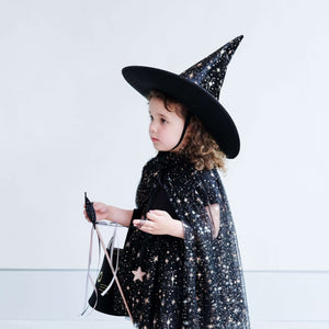 Child wearing Mimi & Lula Aurora Witch Cape and hat, holding Halloween accessories, perfect for magical dress-up and Halloween fun.