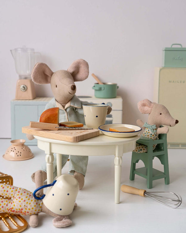 Adorable Maileg mice enjoying a meal, with one mouse sitting in a mint highchair at a cozy kitchen table.