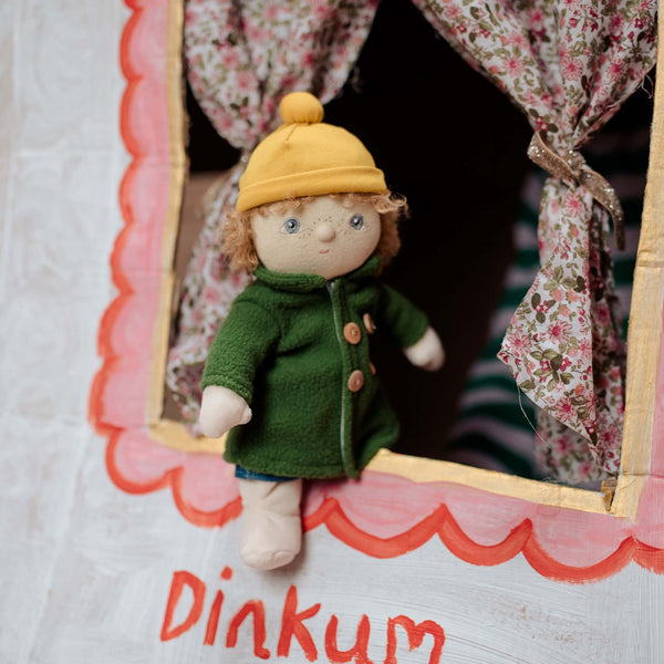 Olli Ella Dress Me Dinky Charlie Chestnut doll peeking out from a colorful playhouse window, wearing a yellow beanie and green coat.