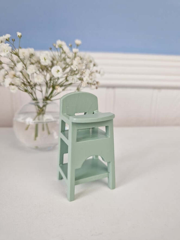 Mint green Maileg wooden high chair for baby mice and MY rabbits, with white flowers in the background.