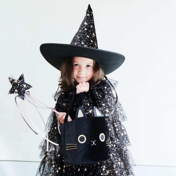 Child in black sparkly witch costume and hat holding a magic wand and cat-shaped bag