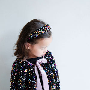 Little girl wearing Mimi & Lula Jazzy Sequin Alice headband and matching sequin outfit with a pink bow.