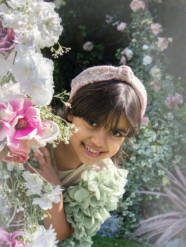 Girl wearing Rockahula sequin knotted headband surrounded by flowers in a garden