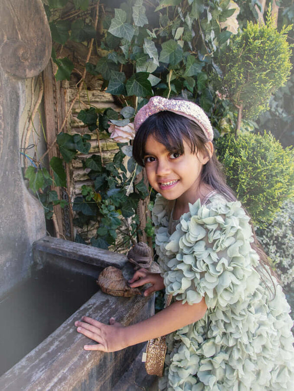 Girl wearing Rockahula sequin knotted headband in garden, adding a touch of sparkle and style with pastel pink sequins.